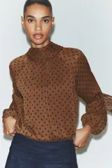 Blusa de cuello subido con diseño de lunares, manga larga abullonada con puños elásticos y forro interior.