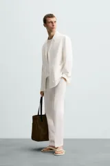 Blazer color blanco confeccionado en tejido con mezcla de algodón y lino, de corte recto y holgado. Tiene cuello con solapas de muesca, manga larga con puños abotonados, bolsillos frontales de parche y cierre frontal con botones.