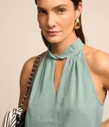 Blusa sin mangas color verde menta, confeccionada en tejido jacquard con textura de pequeños cuadros. Presenta un cuello halter que se anuda o cruza en la parte delantera, creando un escote en V con un recorte central.