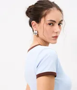 Remera tipo baby tee de corte ajustado y manga corta, en color beige claro, con ribetes en tono marrón oscuro en el cuello redondo y los puños.