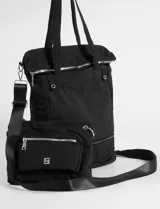 Mochila shopper de color negro, confeccionada en poliéster. Presenta un diseño multifuncional con correas ajustables y removibles que permiten usarla como mochila, cartera cruzada o de hombro. Incluye un compartimento inferior extensible mediante cierre y un bolsillo frontal removible que funciona como estuche independiente.
