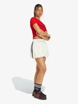 Falda corta tipo balloon de color blanco, con diseño de volumen y las icónicas tres tiras laterales en negro. Presenta el logo del trébol bordado en la parte inferior.