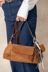 Cartera de gamuza color beige con correa ajustable de cuero sintético marrón, bolsillo frontal con solapa y cierre superior.