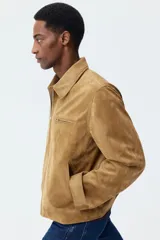 Campera de gamuza sintética color tostado, con cuello camisero, cierre frontal, bolsillo superior con cierre y bolsillos laterales ribeteados.