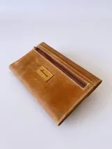 Billetera tipo sobre confeccionada en cuero color camel, con solapa en punta y detalle de costura decorativa en forma de espiga. Cuenta con cierre de broche y monedero externo.