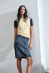 Falda de denim azul con tiro medio, cierre frontal completo con cremallera y detalles de bolsillos falsos con cremalleras en la parte delantera.