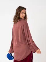Camisa de raso color bordó con silueta suelta, manga larga, puños anchos y cierre frontal con botones a tono.