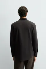 Camisa de corte slim fit, color negro, con cuello italiano, manga larga con puños abotonados y cierre frontal de botones. Confeccionada en tejido de fácil cuidado que minimiza la necesidad de planchado.