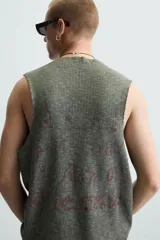 Camiseta sin mangas de punto acanalado, color verde oliva desgastado, con cuello redondo y abertura frontal en forma de 'V'. Presenta un estampado desvanecido en el centro del pecho.