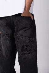 Jean de corte baggy y fit oversize, confeccionado en denim de algodón con lavado efecto gastado en color gris oscuro. Presenta costuras reforzadas en la zona de las rodillas y diseño de cinco bolsillos.