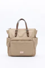 Mochila de poliéster texturizado color beige, con diseño acanalado. Cuenta con asas superiores en color marrón, tiras regulables para la espalda, bolsillo frontal con cierre metálico, compartimentos laterales y un interior amplio.