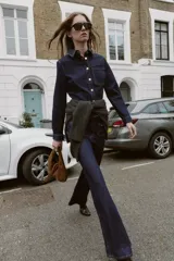 Camisa entallada de denim azul oscuro con cuello solapa, manga larga y cierre frontal con botones metálicos. Presenta un bolsillo de plastrón en el pecho y costuras a contratono.