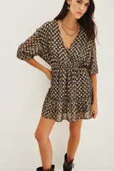 Vestido corto de escote en V cruzado, con mangas tres cuartos y cintura elástica. Presenta un diseño estampado con motivos geométricos en tonos oscuros y detalles metalizados, con un ruedo con volado.