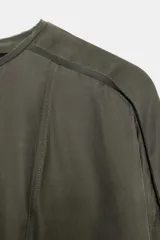 Blusa fluida de color verde oliva oscuro, con cuello redondo y mangas largas abullonadas. Presenta un diseño con bajo elástico y cierre posterior con abertura y botón.