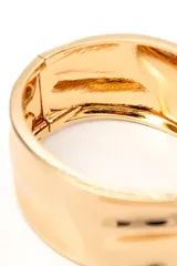 Brazalete rígido color dorado de diseño ancho y superficie con textura ligeramente irregular.