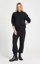 Pantalon tipo jogger de tiro alto, color negro, confeccionado en tejido de punto. Presenta una cinturilla elástica ancha con cordón ajustable y detalle de superposición de encaje en la parte delantera. Cuenta con bolsillos laterales ribeteados, perneras ligeramente holgadas y puños ajustados con elástico.