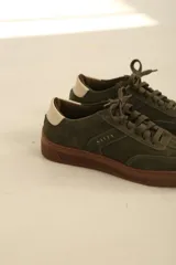 Zapatillas de gamuza en color verde oliva, con suela de goma color marrón y detalle de talón en contraste color crema.