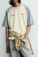 Camiseta de corte relajado con mangas ranglán en color gris y cuerpo en color beige. Presenta cuello redondo, costuras a contraste y detalles de parches y bordados en el pecho.