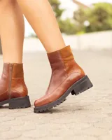 Botas de cuero color marrón, hechas a mano, con suela track negra y cierre lateral. Presentan detalles en gamuza y textura de reptil en los laterales.