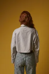 Camisa corta a rayas verticales grises y blancas, con cuello clásico, cierre frontal con botones y mangas largas con puños abotonados.