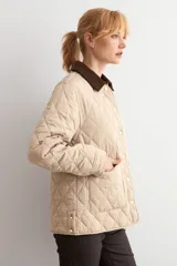 Campera capitoneada de diseño acolchado con patrón de rombos, color beige claro. Presenta cuello camisero de pana en color marrón oscuro, cierre frontal con botones metálicos y bolsillos frontales de parche.