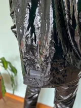 Camisa negra de charol con cuello clásico, cierre frontal con botones y bolsillos de parche en el pecho.