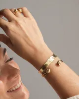 Brazalete rígido abierto de metal color plateado, con terminaciones en forma de herradura.