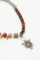 Choker con cadena de piedras y piezas circulares de diferentes tamaños y tonos, incluyendo cuentas rojas, naranjas, lilas, verdes y negras. Presenta detalles de púas doradas y un dije central en forma de escudo de metal grabado.