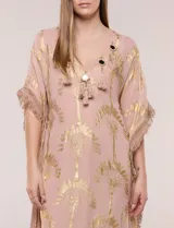 Vestido midi tipo túnica de silueta holgada, marca America & Beyond, color rosado con estampado metalizado dorado de palmeras. Cuenta con escote en V, detalles de borlas, espejos y apliques decorativos, y flecos en mangas, laterales y ruedo.