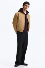 Campera bomber de nylon color tostado, con cuello, puños y bajo acanalados. Presenta cierre frontal, bolsillos laterales con botón a presión y un bolsillo con cierre en la manga.
