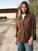 Camisa marrón de lana con cuello camisero, cierre frontal con botones y bolsillos de parche con apliques de tejido artesanal. Manga larga con puños abotonados y corte holgado.