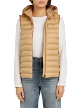 Chaleco acolchado color beige con capucha desmontable, cierre frontal con cremallera, dos bolsillos laterales con cremallera y logo de Tommy Hilfiger bordado en el pecho. Confeccionado en poliéster reciclado con acabado repelente al agua.
