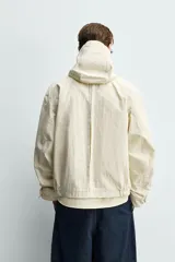 Parka cropped fit de tejido técnico ligero color beige, sin forro interior, con cuello solapa, capucha desmontable y manga larga. Cuenta con bolsillos de solapa en la cadera y cierre frontal con cremallera oculta por solapa con botones a presión.