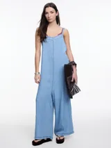 Enterito de denim suave confeccionado en 100% lyocell, con escote recto y breteles finos regulables que se ajustan en la espalda. Presenta una silueta amplia de pierna recta, caída fluida, bolsillos traseros aplicados y costuras a contratono.