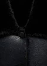 Chaqueta de doble faz con exterior de cuero sintético negro y forro interior de pelo sintético al tono. Presenta cuello camisero, cierre frontal con botones, manga larga y dos bolsillos de parche delanteros.