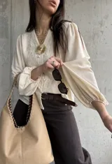 Camisa beige de manga larga con diseño abullonado y puños elastizados, escote en V con botones frontales y sutiles bordados florales tono sobre tono.