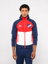Campera deportiva Umbro del Club Nacional de Football, modelo Summit. Presenta un diseño con bloques de color en azul, rojo y blanco, con capucha, cierre frontal y bolsillos laterales con cierre. Incluye el logo de la marca y el escudo del club en el pecho.