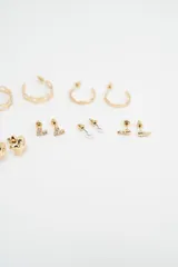 Set de caravanas compuesto por múltiples pares de aros en tono dorado, incluyendo aros tipo argolla de diferentes tamaños, aros con perlas pequeñas, aros con formas geométricas y aros con cristales engarzados.