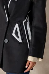 Tapado de paño negro con detalles de costuras y bordes en color blanco. Presenta un diseño de doble botonadura, solapas clásicas y corte amplio.