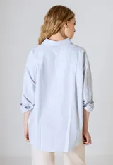 Camisa blanca de corte clásico, con cuello camisero y mangas largas con puños abotonados.