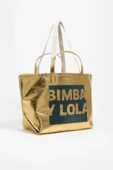 Bolso tipo tote de Bimba y Lola, color dorado con acabado metalizado y efecto arrugado. Presenta un diseño cuadrado con estampado central de la marca en un recuadro oscuro y doble asa de mano en color crema.