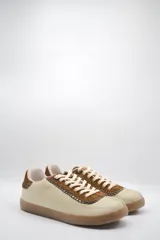 Zapatillas bajas de cuero color crema con detalles en marrón y cordones blancos.
