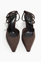 Zapatos de tacón tipo pump confeccionados en satén color marrón oscuro. Presentan un diseño de punta fina, taco de carrete revestido y una pulsera ajustable con hebilla metálica que rodea el tobillo.