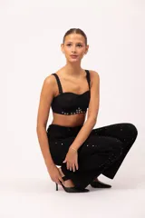 Top tipo corset negro con copas armadas y diseño drapeado en el busto. Presenta una base curva decorada con ojalillos metálicos y tachas plateadas. Incluye breteles intercambiables y cierre posterior con ganchos regulables.