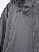 Campera gris con capucha con borde de piel sintética, cierre frontal con cremallera, bolsillos laterales con solapa y bolsillo con cremallera en la manga.