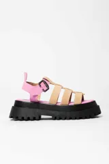 Sandalia tipo gladiadora con plataforma track negra. Presenta un diseño bicolor con tiras delanteras en color amarillo neón y talón con tira ajustable en color beige. Incluye hebilla metálica negra.