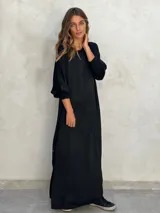 Vestido largo negro de corte holgado, con mangas largas abullonadas y puños ajustados.