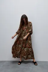 Vestido largo de silueta amplia y caída fluida, con estampado y recortes fruncidos que aportan movimiento. Presenta escote con abertura, cierre frontal con botones y mangas largas de volumen amplio con puños elastizados.