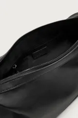 Bolso tipo bandolera de color negro, con compartimento principal con cierre de cremallera y bolsillo interior. Presenta un asa de hombro ajustable y un detalle decorativo de charms colgantes en uno de los laterales.