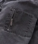 Chaqueta de denim color gris con acabado estonado, cierre frontal con cremallera, cuello camisero y manga larga. Presenta un estampado con la palabra 'OUTLAW' en tipografía gótica en el pecho y un bolsillo con cierre en la manga izquierda.